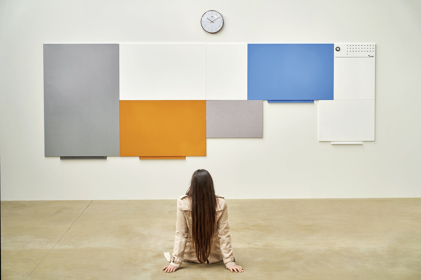 Woman sitting in front of a large modular frameless whiteboard installation composed of colourful interconnected panels – ideal for creative planning, collaboration, and customisable workspace design.